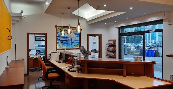 Ufficio con bancone in legno, sedie arancioni, lampade a sospensione, quadro con barca a vela e vetrata d'ingresso