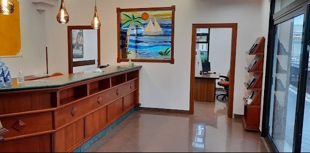 Bancone di accoglienza in legno con piano verde, lampade a sospensione e vetrata colorata con veliero e palma