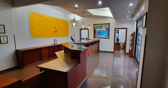 Reception con bancone in legno scuro, pannello giallo alla parete, lampade a sospensione e pavimento lucido