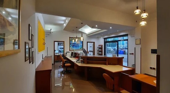 Ufficio con bancone in legno ad angolo, sedie arancioni, lampade a sospensione e vetrata d'ingresso sulla strada